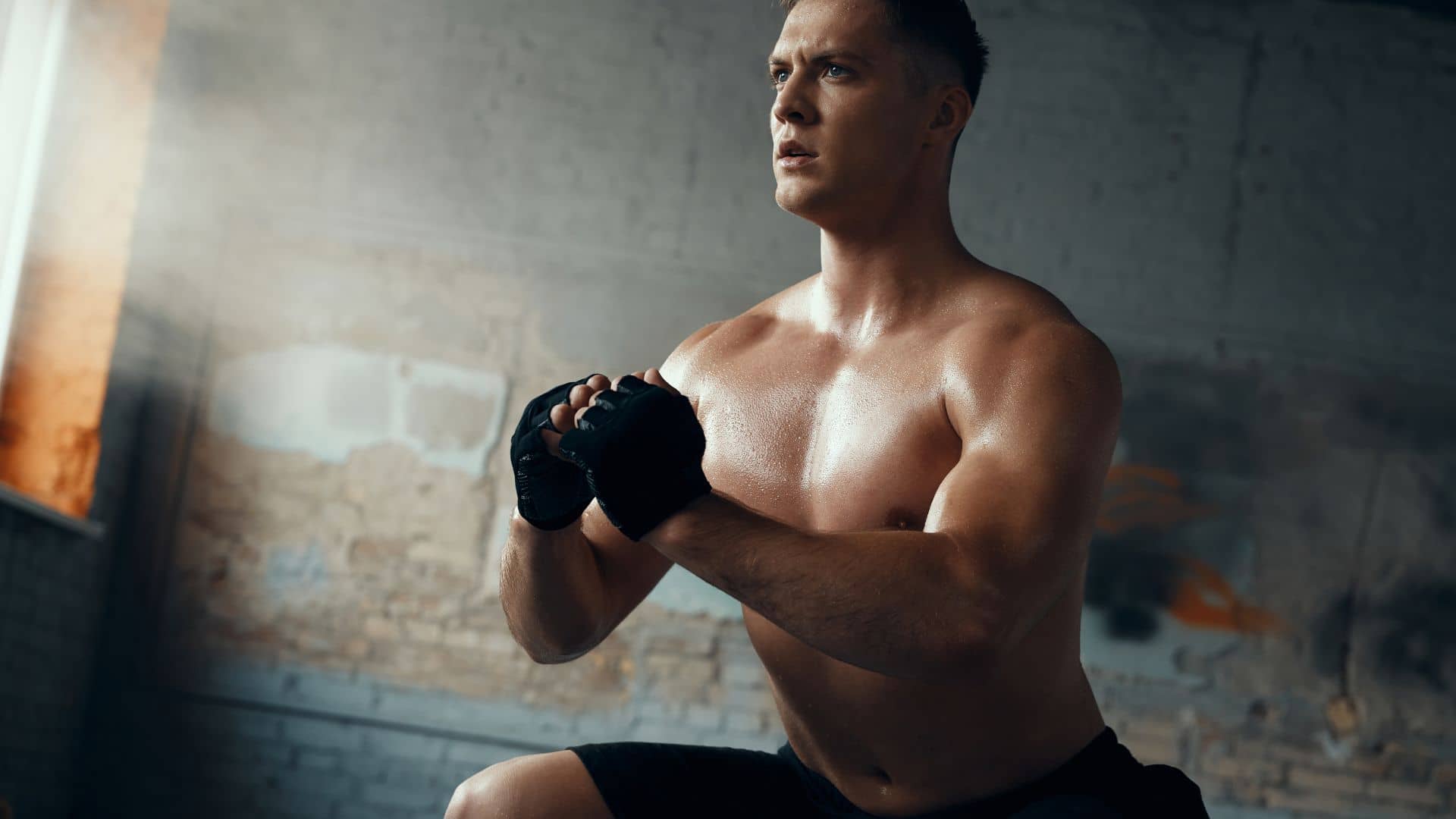 Confident young man standing in squatting position while training in gym