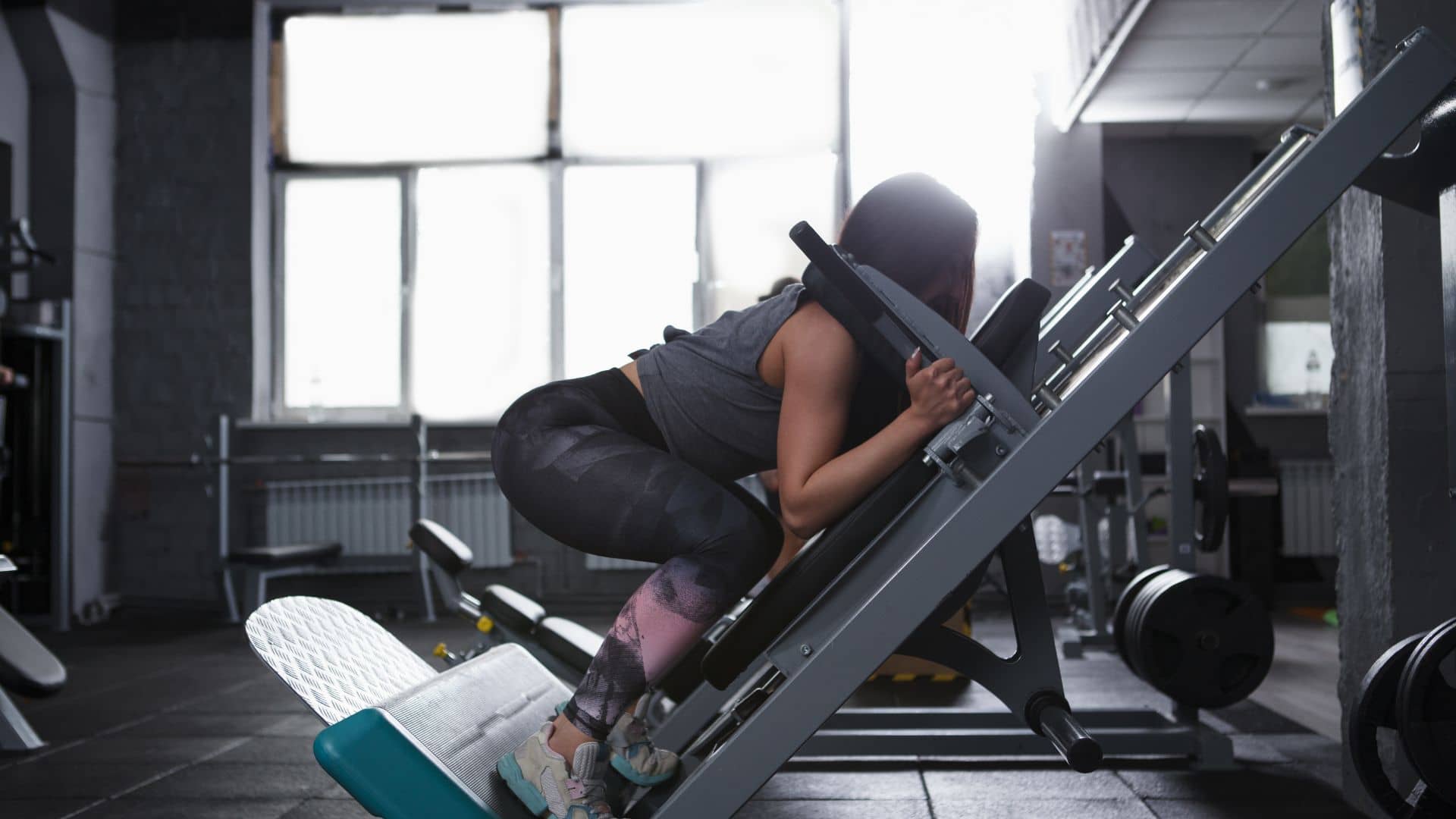 Profile shot of a strong athletic woman doing squats in hack squat gym machine