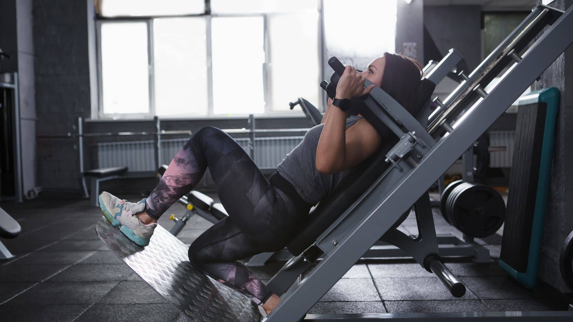 Female athlete doing lunges in hack squat gym machine, copy space