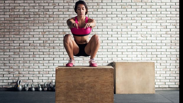 Concentrated woman squatting over a plyo box