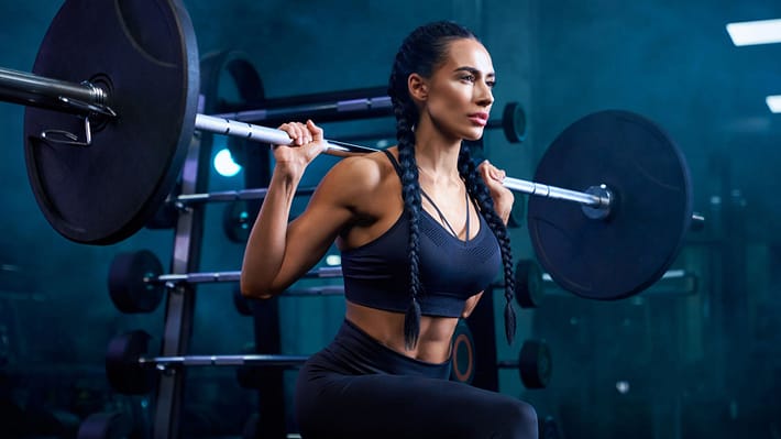 Woman doing bulgarian squats using barbell in gym.