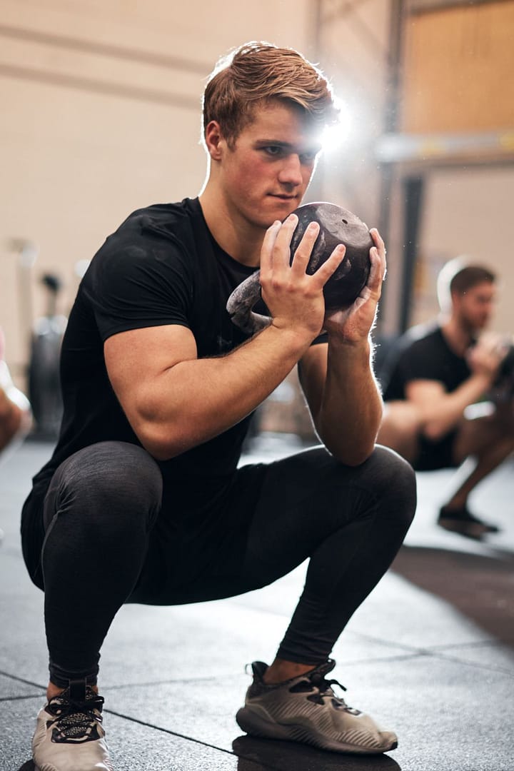 Man exercising at home doing kettlebell squat in living room