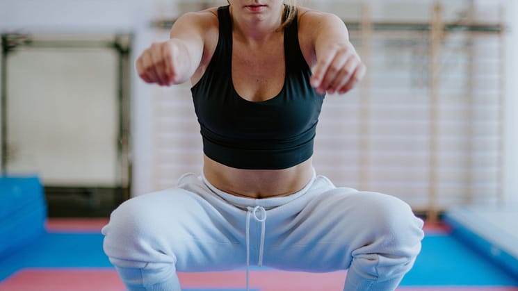 Sportswoman squatting with arms outstretches